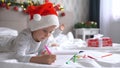 Two cute little girls sisters wearing Santa Helper hats write letter to Santa lying on bed at home in Christmas