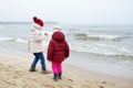 Two cute little sisters having fun together at winter beach on cold winter day. Kids playing by the ocean. Royalty Free Stock Photo