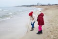 Two cute little sisters having fun together at winter beach on cold winter day. Kids playing by the ocean. Royalty Free Stock Photo