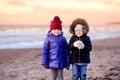 Two cute little sisters having fun together at winter beach on cold winter day. Kids playing by the ocean. Royalty Free Stock Photo