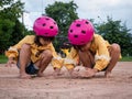 Two cute little sisters in helmets are playing with sand in park on a sunny summer day, taking a break after cycling practice.