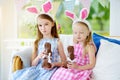 Two cute little sisters wearing bunny ears eating chocolate Easter rabbits. Kids playing egg hunt on Easter. Royalty Free Stock Photo