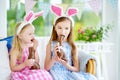 Two cute little sisters wearing bunny ears eating chocolate Easter rabbits. Kids playing egg hunt on Easter. Royalty Free Stock Photo