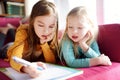 Two cute little sisters writing a letter together at home. Older sister helping youngster with her homework.