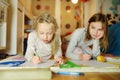 Two cute little sisters writing letters together at home. Older sister helping youngster with her homework