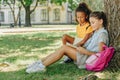 Cute multicultural schoolgirls sitting on lawn under tree and reading book together Royalty Free Stock Photo