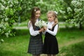 Two cute schoolgirl girls in an apple blossoming garden after school. End of school year