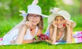 Two cute sisters or friends in a picnic garden lie on a deck and eat freshly picked cherries