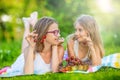 Two cute sisters or friends in a picnic garden lie on a deck and eat freshly picked cherries