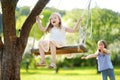 Two cute sisters having fun on a swing in blossoming old apple tree garden outdoors on sunny spring day. Royalty Free Stock Photo