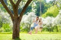 Two cute sisters having fun on a swing in blossoming old apple tree garden outdoors on sunny spring day Royalty Free Stock Photo
