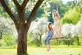 Two cute sisters having fun on a swing in blossoming old apple tree garden outdoors on sunny spring day Royalty Free Stock Photo