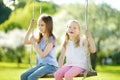 Two cute sisters having fun on a swing in blossoming old apple tree garden outdoors on sunny spring day. Royalty Free Stock Photo