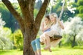 Two cute sisters having fun on a swing in blossoming old apple tree garden outdoors on sunny spring day. Royalty Free Stock Photo