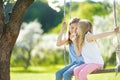 Two cute sisters having fun on a swing in blossoming old apple tree garden outdoors on sunny spring day Royalty Free Stock Photo