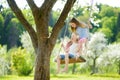 Two cute sisters having fun on a swing in blossoming old apple tree garden outdoors on sunny spring day Royalty Free Stock Photo