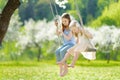 Two cute sisters having fun on a swing in blossoming old apple tree garden outdoors on sunny spring day Royalty Free Stock Photo