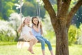 Two cute sisters having fun on a swing in blossoming old apple tree garden outdoors on sunny spring day Royalty Free Stock Photo