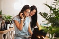Two cute slim girls with long dark hair,wearing casual style,sit at the table and look attentively at the laptop screen Royalty Free Stock Photo