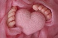 Two cute tiny baby feet wrapped in pink knitted blanket. And a knitted heart made of woolen threads. Royalty Free Stock Photo