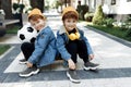 Two cute twin boys with happy faces sitting on the skateboard or pennyboard in the street.