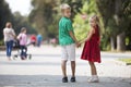 Two cute young blond smiling children, girl and boy, brother and sister holding hands on blurred bright sunny summer park alley Royalty Free Stock Photo