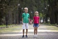 Two cute young blond smiling children, girl and boy, brother and sister holding hands on blurred bright sunny summer park alley Royalty Free Stock Photo