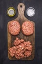 Two cutlets for burgers with minced meat on a cutting board with herbs, butter and salt wooden rustic background top view close