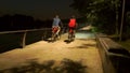 Two cyclists passing by on park embankment at late evening. Slow motion shot