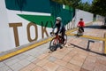 Two Cyclists ride past a large-scale TOKYO 2020 sign at Odaiba Seaside Park venue for Olympic Swimming and Triathlon