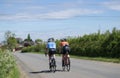 Two cyclists riding a bicycle and talking side by side on a sunny day after the Coronavirus lockdown rules have eased.