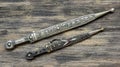 Two daggers with ornate pattern on old wooden background close-up.