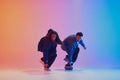 Two dancers performing sync hip-hop moves dressed in denim clothes against gradient background in neon light. Royalty Free Stock Photo