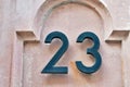 Two dark coloured iron digits fixed on a stone wall and showing the number twenty three