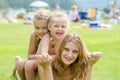 Two daughters are sitting on the mothers back, hot summer day relaxing on the green lawn beautiful beaches