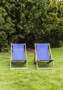 Two deck chairs in a garden with solid trees as a background Royalty Free Stock Photo