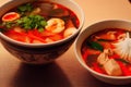 Two deep bowls with Thai tom yam soup with bright tomato sauce and coconut