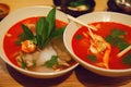 Two deep bowls with Thai tom yam soup with bright tomato sauce and coconut