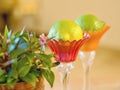 Two delicate glass vessels in delicate colors with flowers to the side and inside a fresh citrusfruit