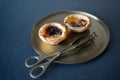 Two delicious Belem cakes Pasteis de Belem on a bronze tray, with serving tongs. Portuguese sweet making tradition.