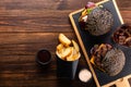 Two delicious black grilled burgers with beef cutlet, a glass of cola and french fries on a wooden board Royalty Free Stock Photo