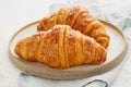 Two delicious croissants on plate and hot drink in mug. Morning French breakfast with fresh pastries. Light gray background