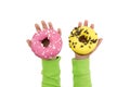 Two delicious donuts with yellow and pink icing in children`s hands isolated on a white background. View from above. Copy of space Royalty Free Stock Photo