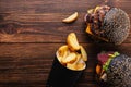 Two delicious grilled black burgers with beef patty and fries on a wooden board, top view. Royalty Free Stock Photo