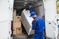 Two Delivery Men Unloading Furniture From Vehicle