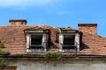 Two destroyed roof windows with rusted metal flower holders on abandoned old building with broken and missing roof tiles Royalty Free Stock Photo