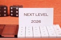 Two dice and a card stating Next Level 2026 are placed on a white calculator. This represents striving for success in future Royalty Free Stock Photo