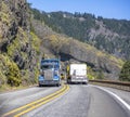 Two different classic loaded big rigs semi trucks with semi trailers moving in opposite directions on the narrow winding road with