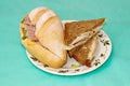 Two different sandwiches of white and black bread on the same plate on a turquoise background. A hearty snack Royalty Free Stock Photo