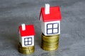 Two different sizes tiny houses on two different height stacks of coins symbolizing different costs Royalty Free Stock Photo